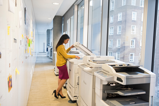 A full length photo of beautiful businesswoman using computer printer.